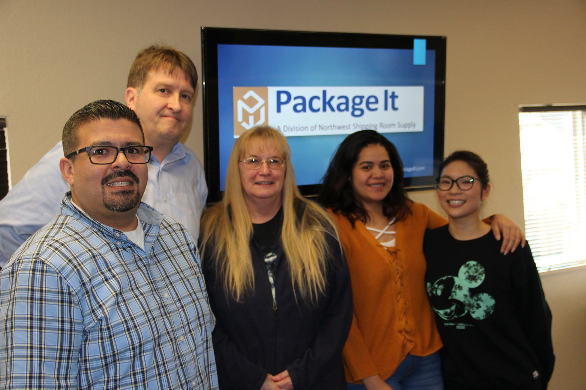 A group of people are posing for a picture in front of a package it sign.