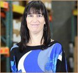 A woman in a blue and black shirt is smiling in a warehouse.