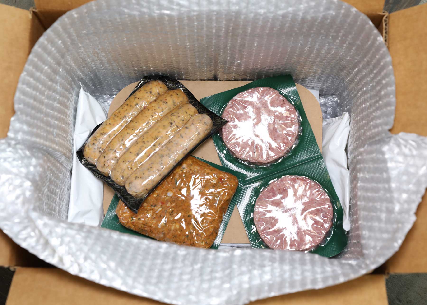 A cardboard box filled with sausages and hamburgers
