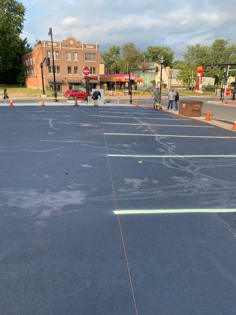 Newly painted blue parking lot with white lines. Workers and buildings in the background.