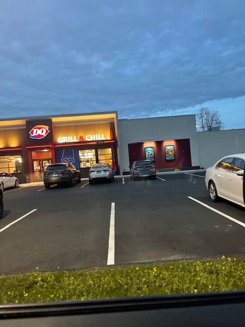 Exterior of a Dairy Queen Grill & Chill restaurant with cars parked in front under a cloudy sky.