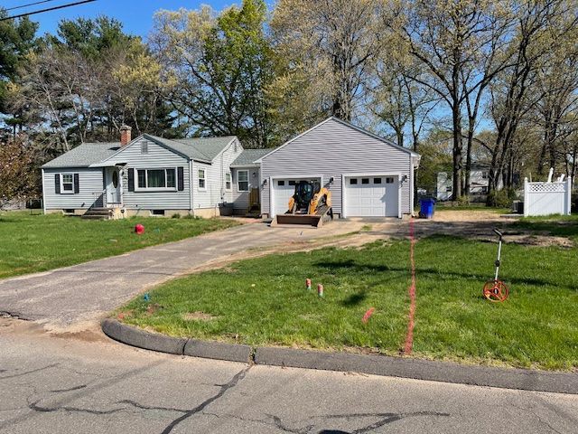A house with a driveway and attached garage; a small excavator sits in front. Sunny day.