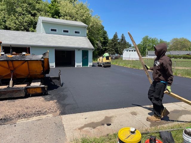 Asphalt driveway paving with a worker smoothing the new surface.