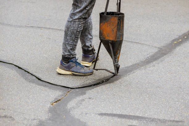 Worker in gray jeans applies sealer to cracked asphalt, showcasing asphalt sealing services.