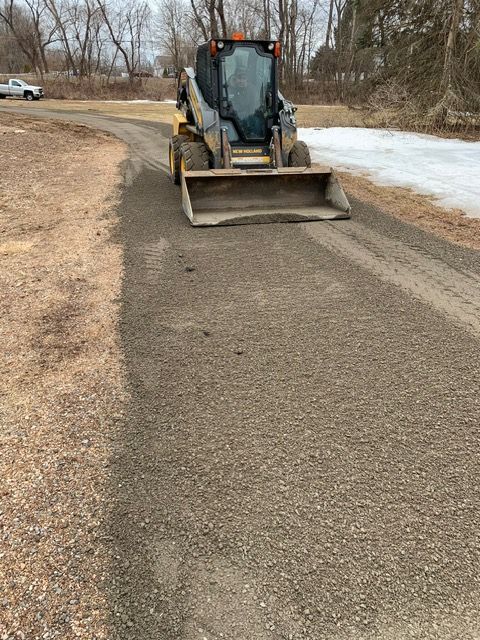 Skid steer compacting gravel on a road. Dark, overcast day.