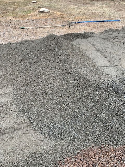 Pile of gravel on a sandy surface near stone pavers.