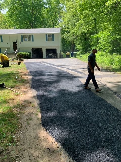 Man walking on newly paved asphalt driveway; house and trees in background.