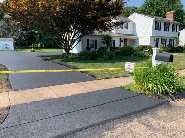 Newly paved driveway, walkway, and curb in front of a two-story white house; caution tape present.
