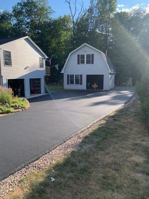 Freshly paved asphalt driveway leading to a white two-car garage and house; sunny day.