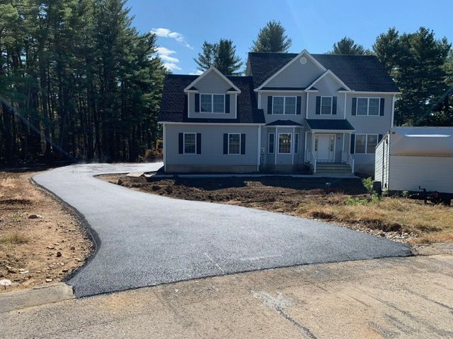A new, two-story house with a freshly paved driveway, surrounded by trees.
