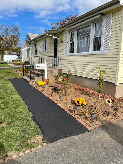 Yellow house with a black pathway, a garden bed with flowers, and a white mailbox.