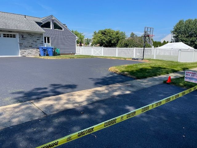 Newly paved driveway with caution tape in front of a house, basketball hoop visible.