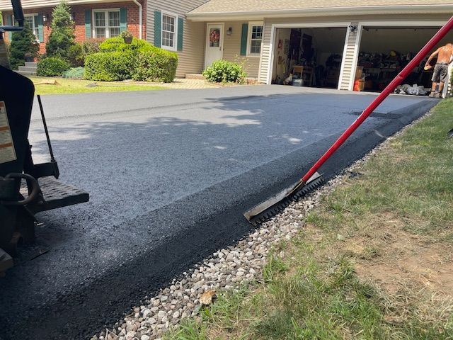 New asphalt driveway being installed next to a grassy area; person using a long-handled tool.