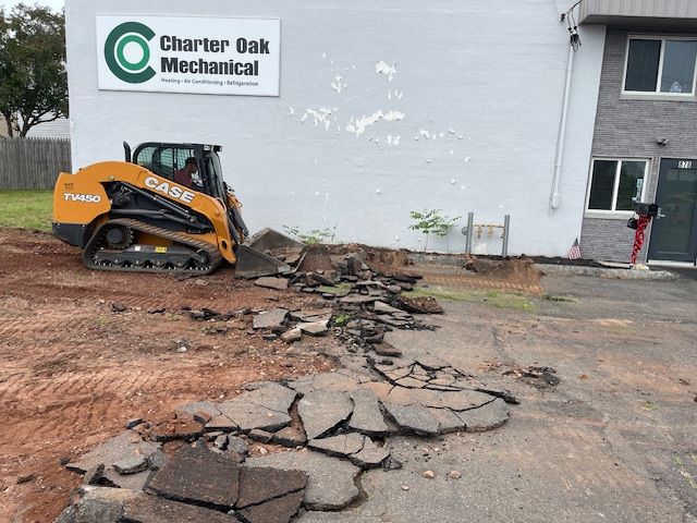 A Case skid steer removing asphalt in front of Charter Oak Mechanical building; dirt and debris are visible.