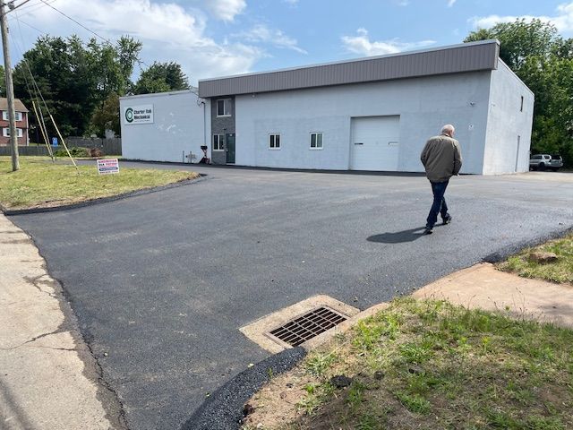 Man walks on newly paved asphalt in front of a light grey commercial building.