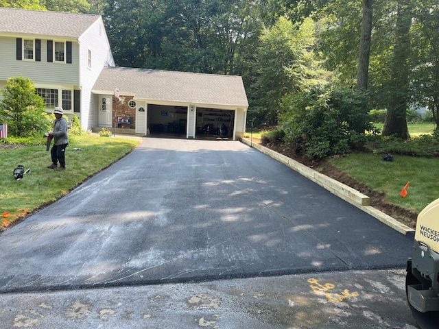 Newly paved asphalt driveway in front of a house with a worker and a roller machine.