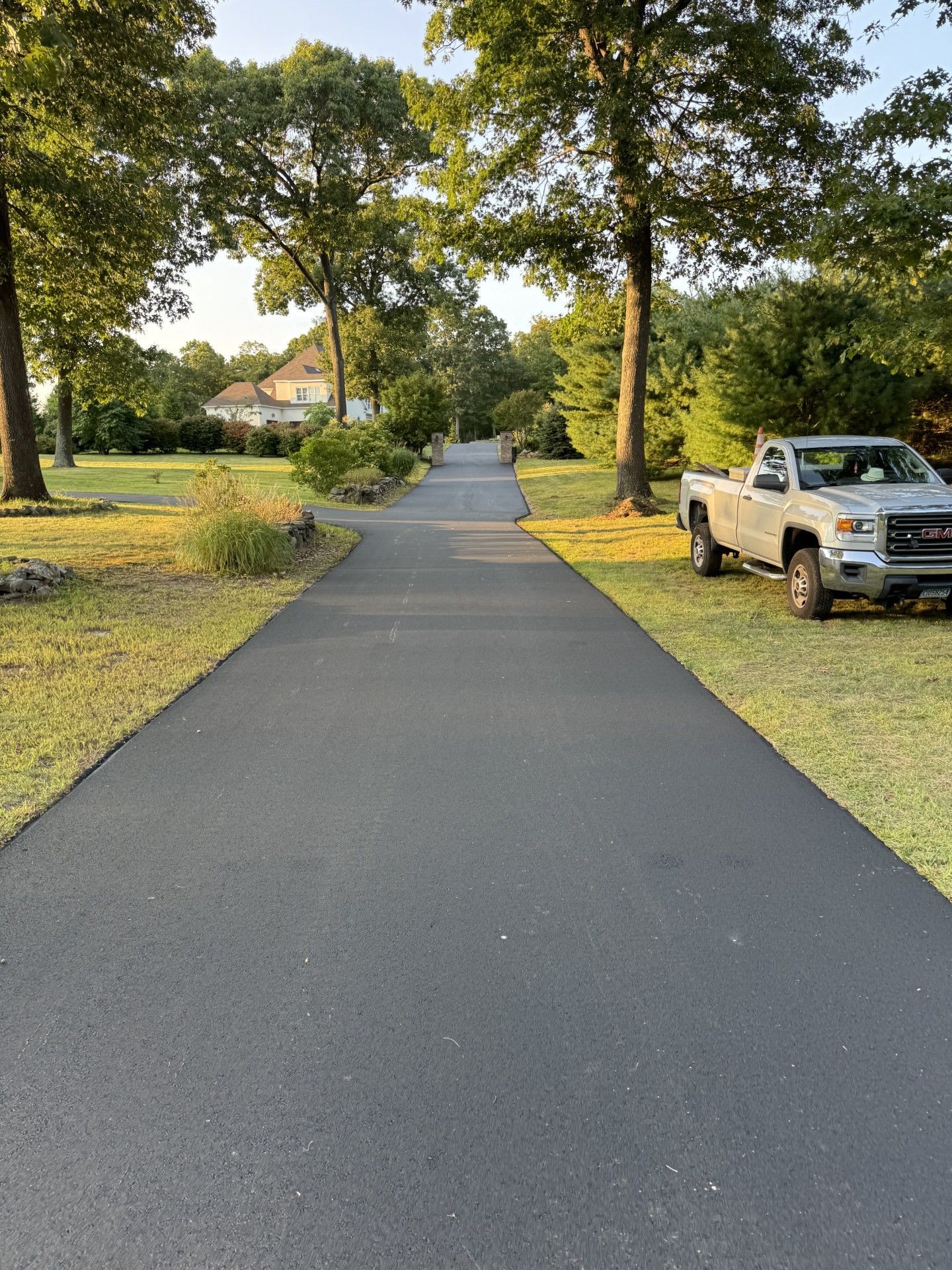 A paved pathway through a grassy area, lined with trees and a parked truck.