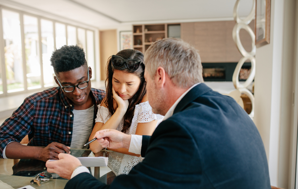 A man in a suit is talking to a young couple at a table.