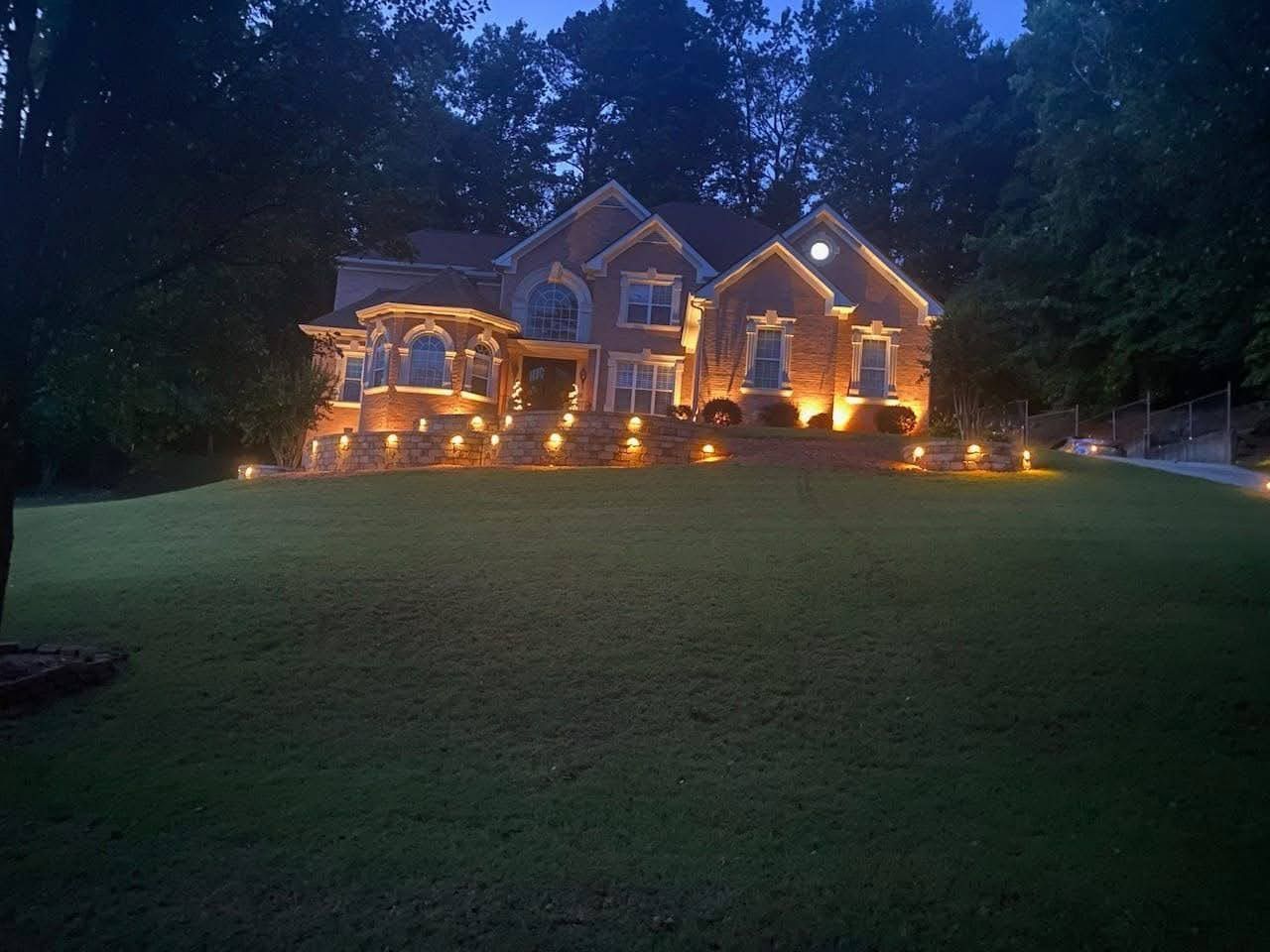 A large house is lit up at night and surrounded by trees