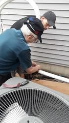 Two men are working on an air conditioner outside of a house.