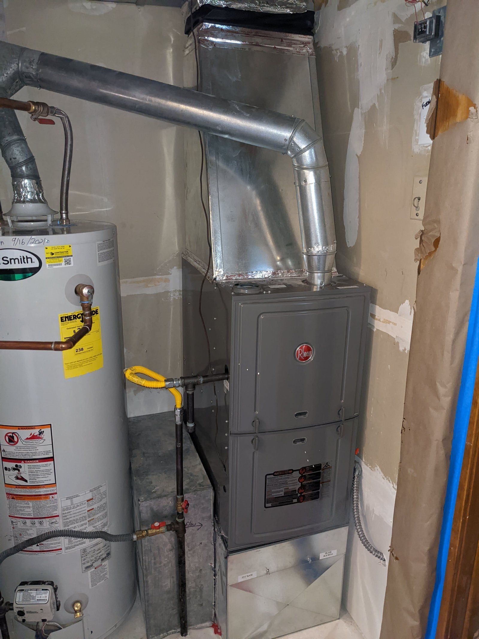 Furnace and water heater in a utility room. Gray metal appliances, ductwork, and a yellow gas line.