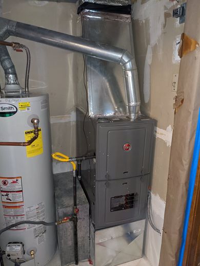 Furnace and water heater in a utility room. Gray metal appliances, ductwork, and a yellow gas line.