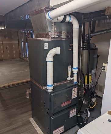 A gas furnace in a basement, with white PVC pipes and metal ductwork.