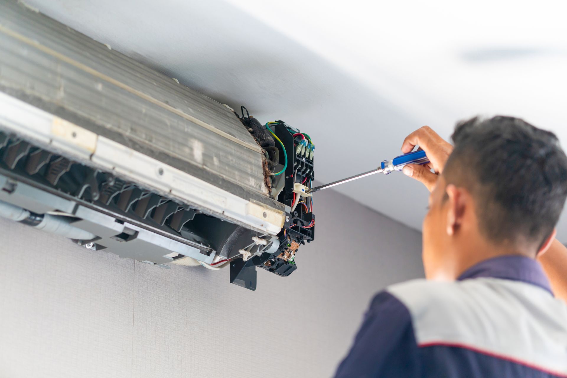 A repairman using a screwdriver on a disassembled, wall-mounted air conditioning unit.