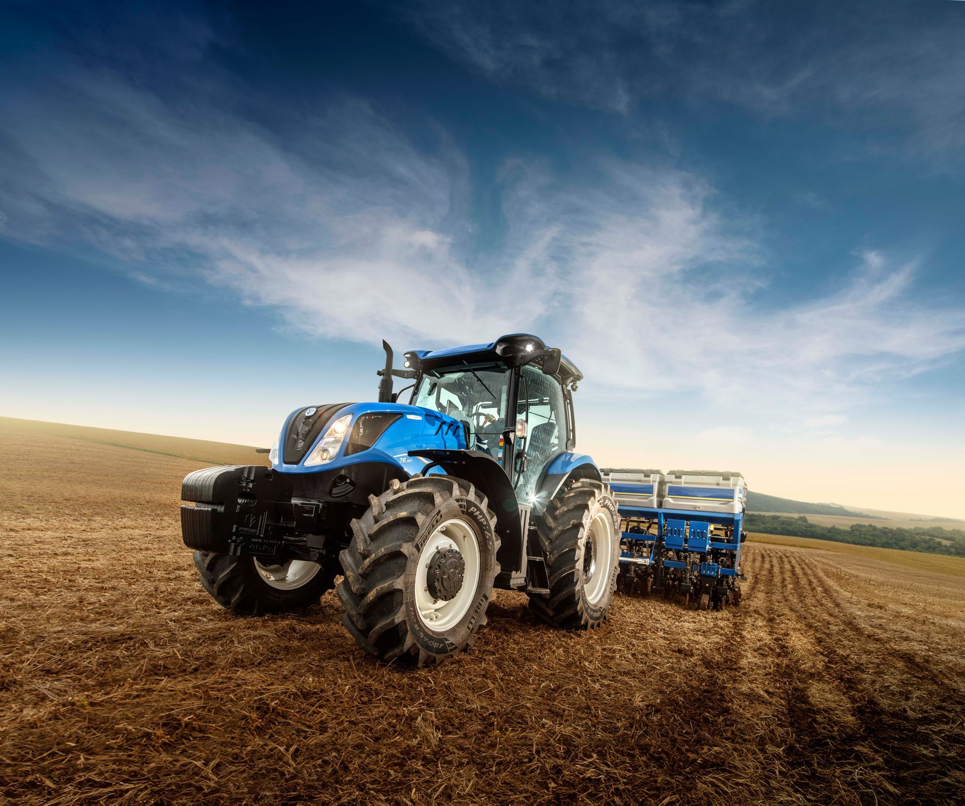 Un tractor agrícola azul está arando un campo con una sembradora acoplada a él.