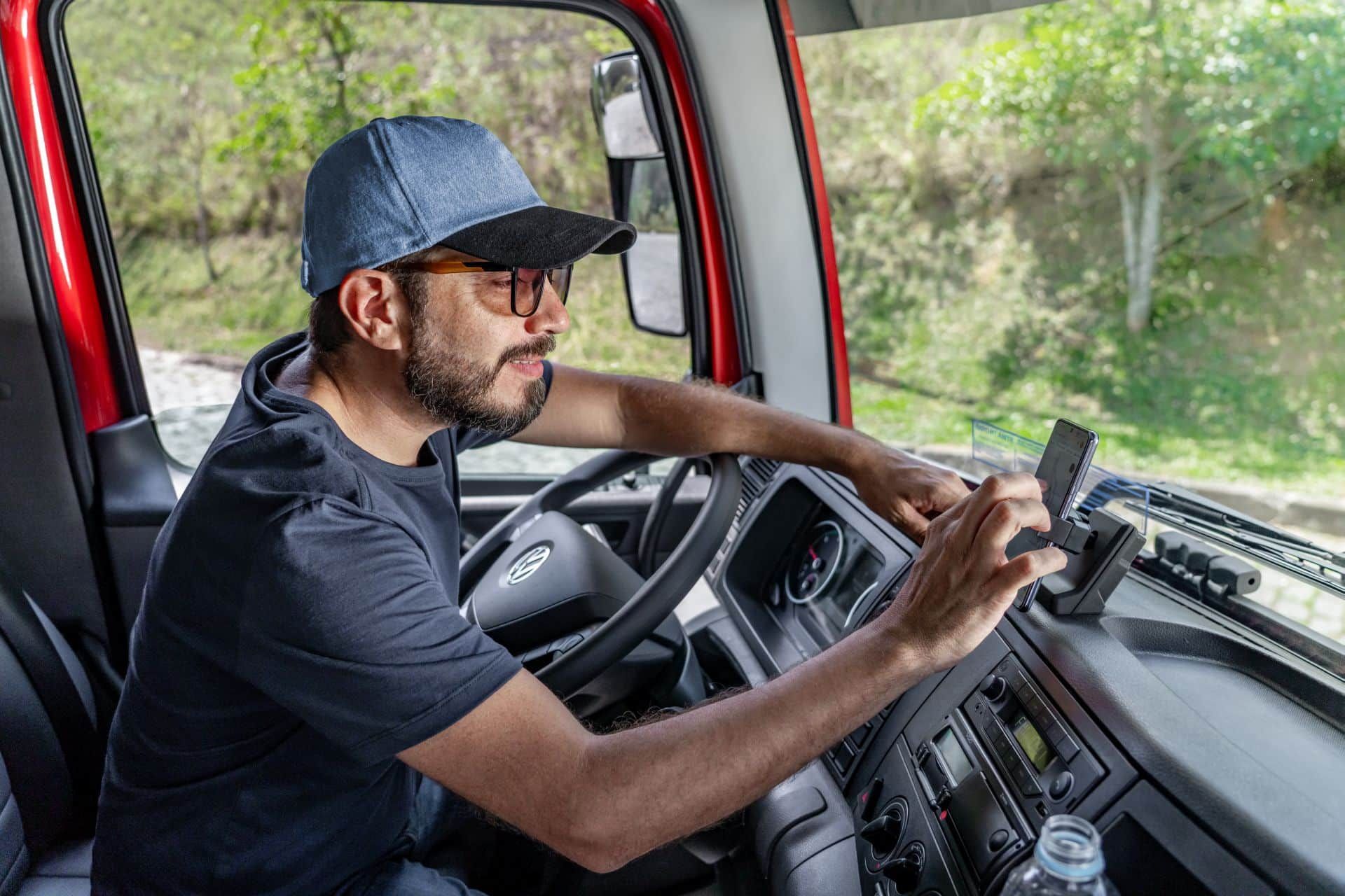 Un hombre está sentado en el asiento del conductor de un camión usando un teléfono celular.