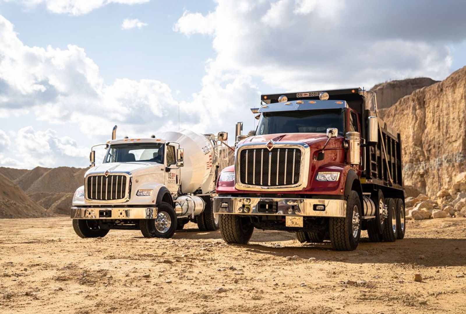 Dos camiones de construcción en un entorno desértico: una hormigonera blanca y un camión volquete marrón.