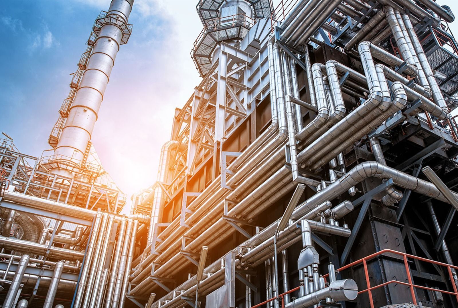 Complejo industrial con tuberías plateadas, tanques y torres contra un cielo brillante.