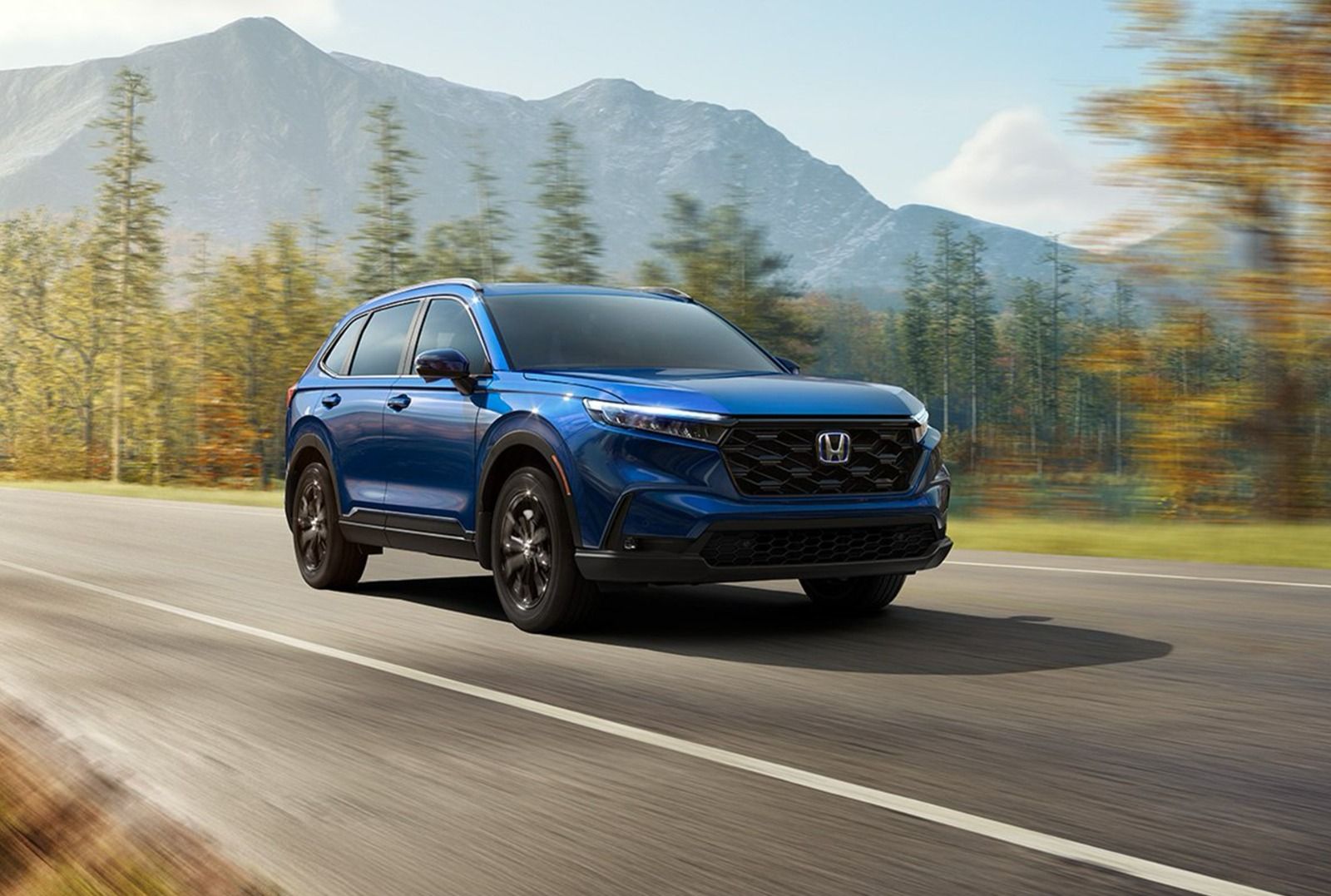 SUV Honda CR-V azul circulando por una carretera con montañas y árboles otoñales al fondo.
