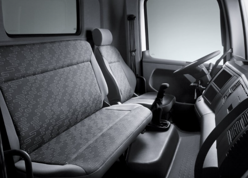 Interior de la cabina de un camión: dos asientos, volante, palanca de cambios y tablero. Blanco y negro.