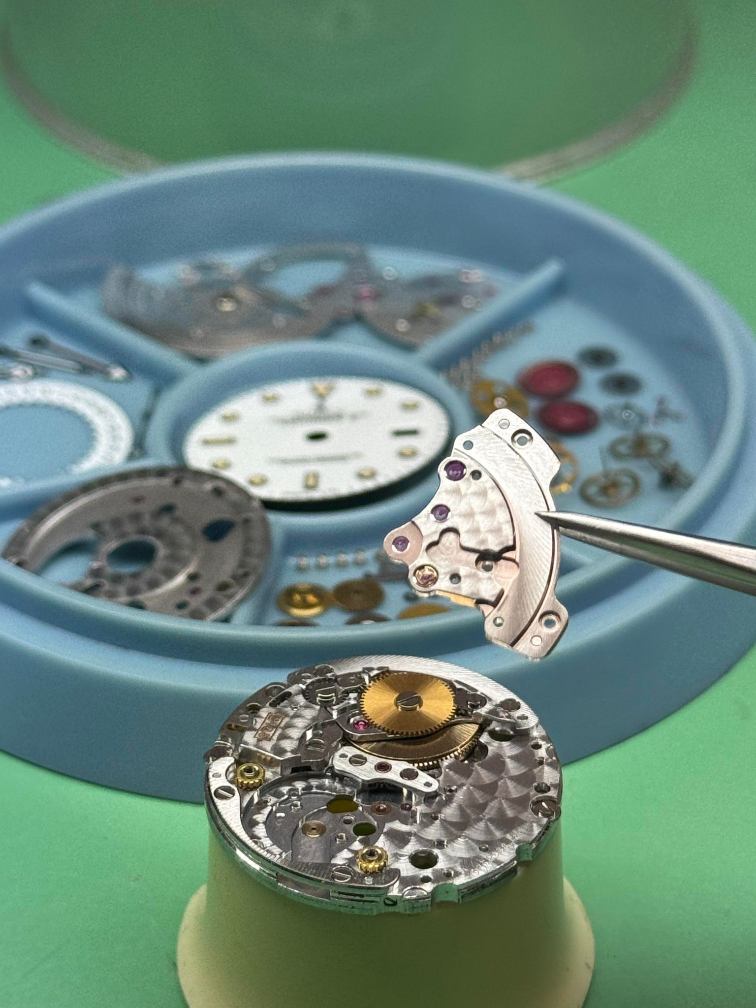 Primo piano di un orologio in riparazione su un tavolo verde.