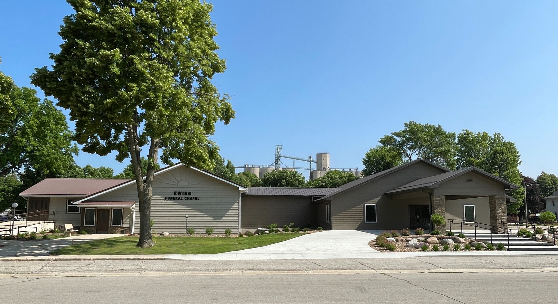 Residential building with a curved facade, trees, and parked cars along a quiet street under a clear blue sky