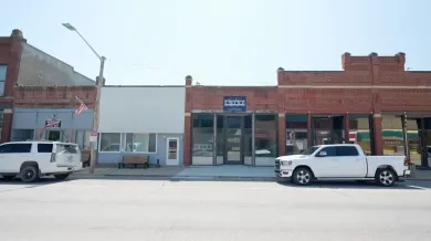 Small brick storefronts on a sunny street, with white pickup trucks parked in front.