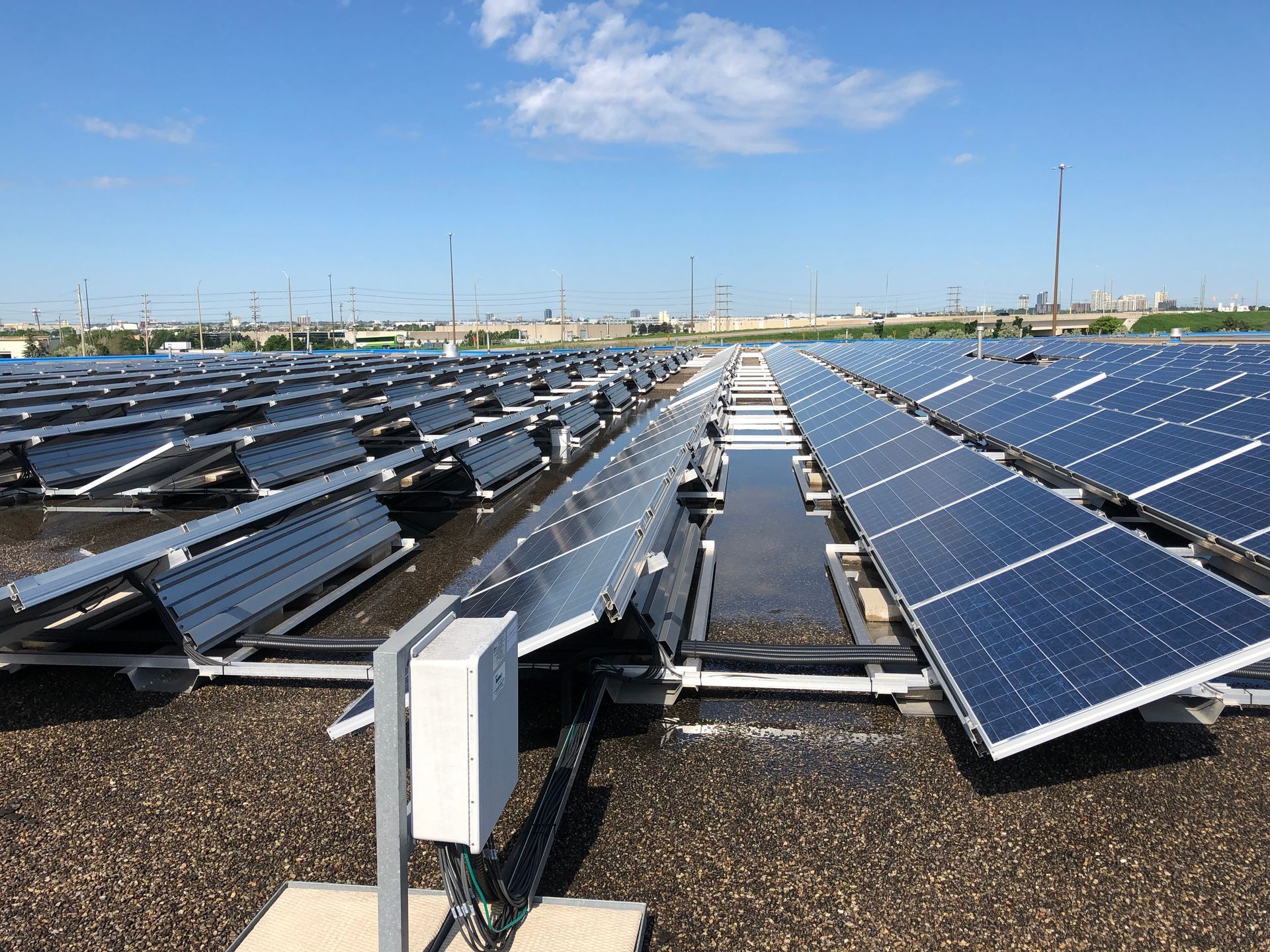 Rows of solar panels installed on a flat, gravel-covered roof under a clear blue sky.