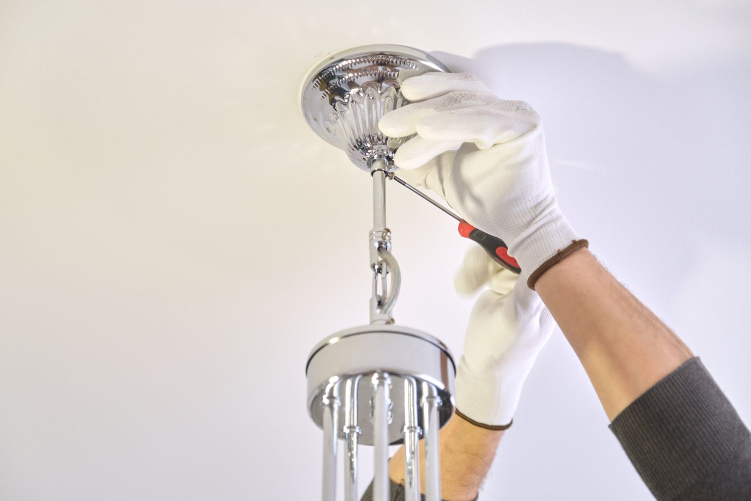 A person is fixing a light fixture with a screwdriver