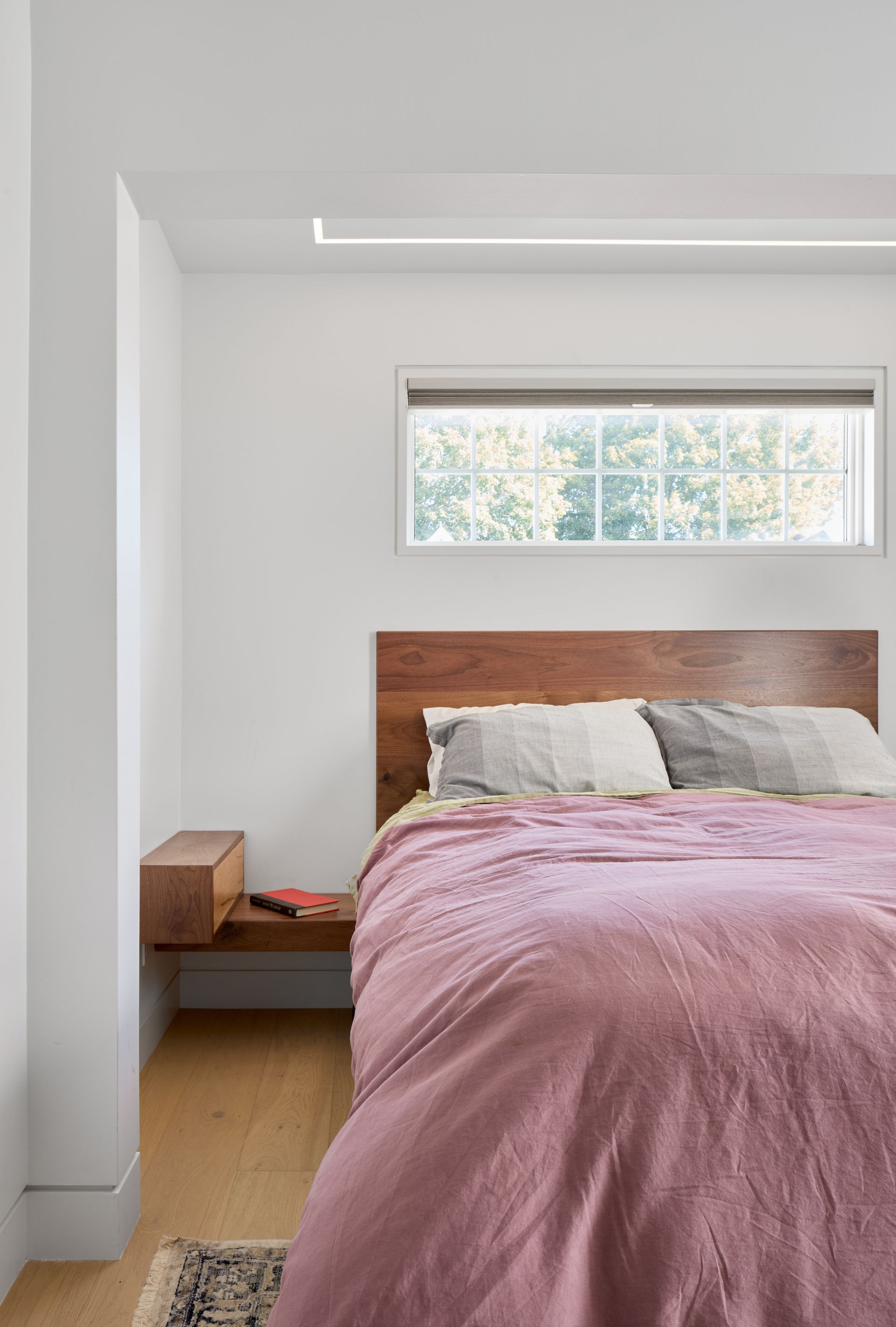 A bedroom with a bed , nightstand , window and pink comforter.