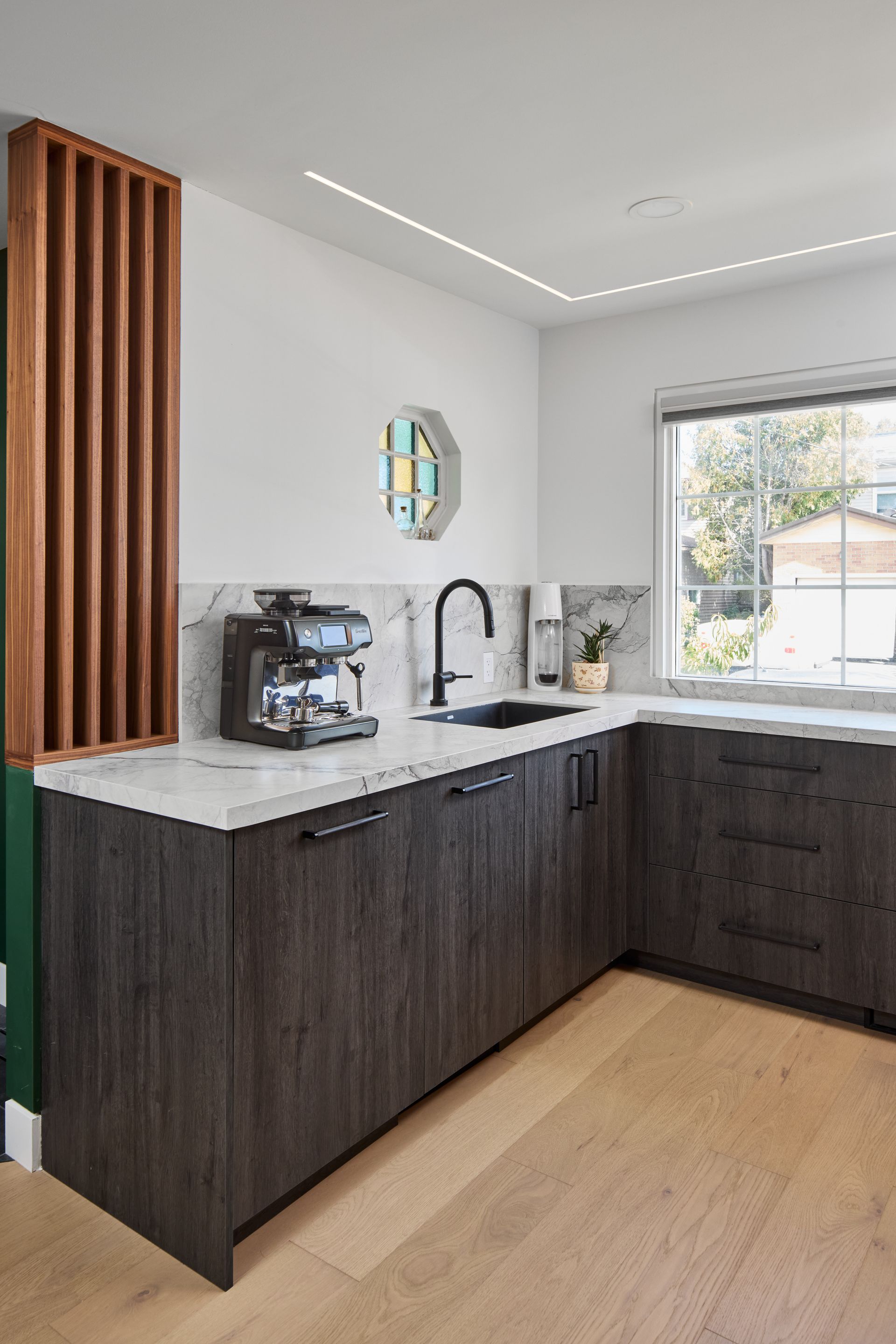 A kitchen with wooden cabinets , a sink , a coffee maker and a window.