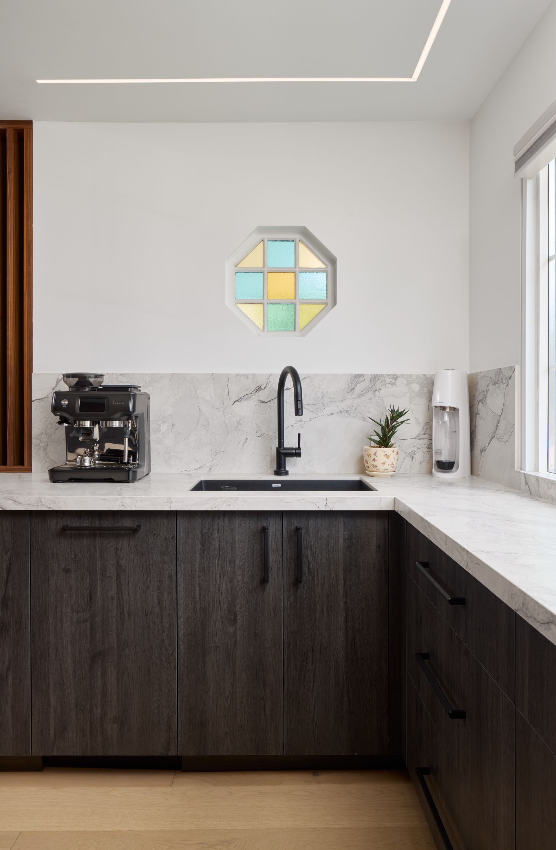 A kitchen with a sink , a coffee maker , and a stained glass window.