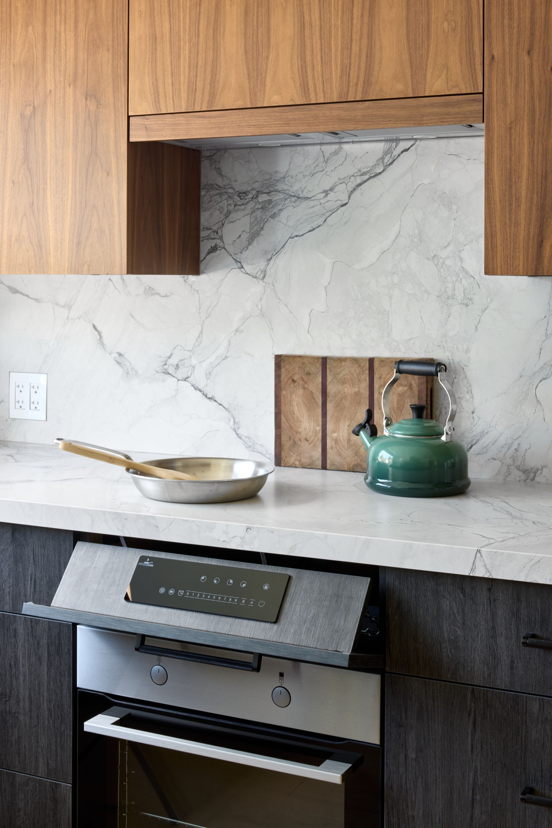 A kitchen with a green tea kettle and a frying pan on the counter.