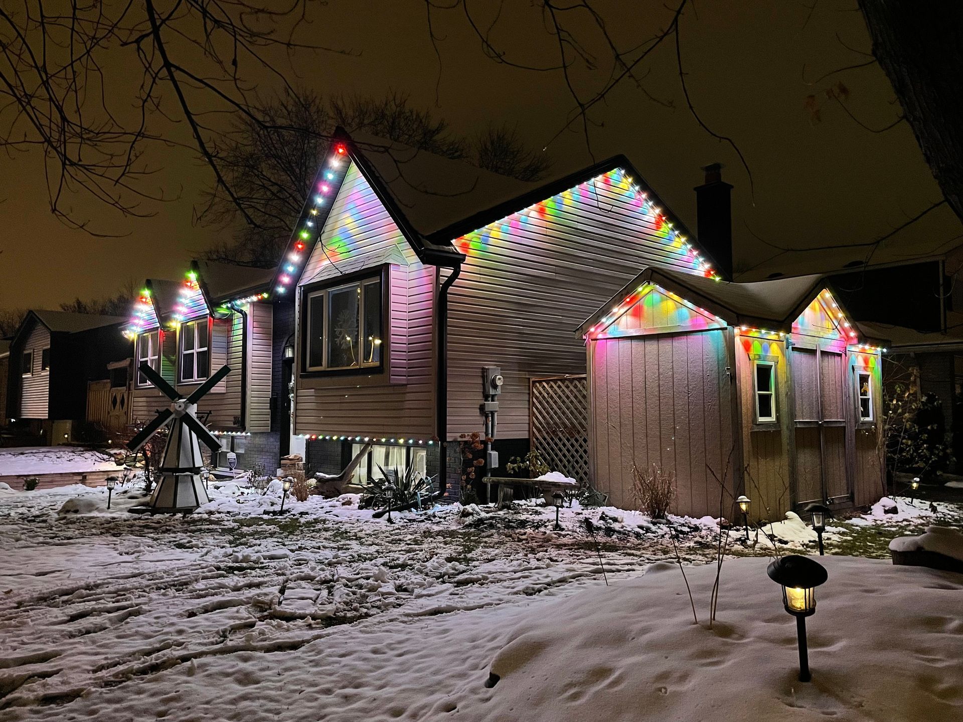 A house with christmas lights on it is covered in snow at night.