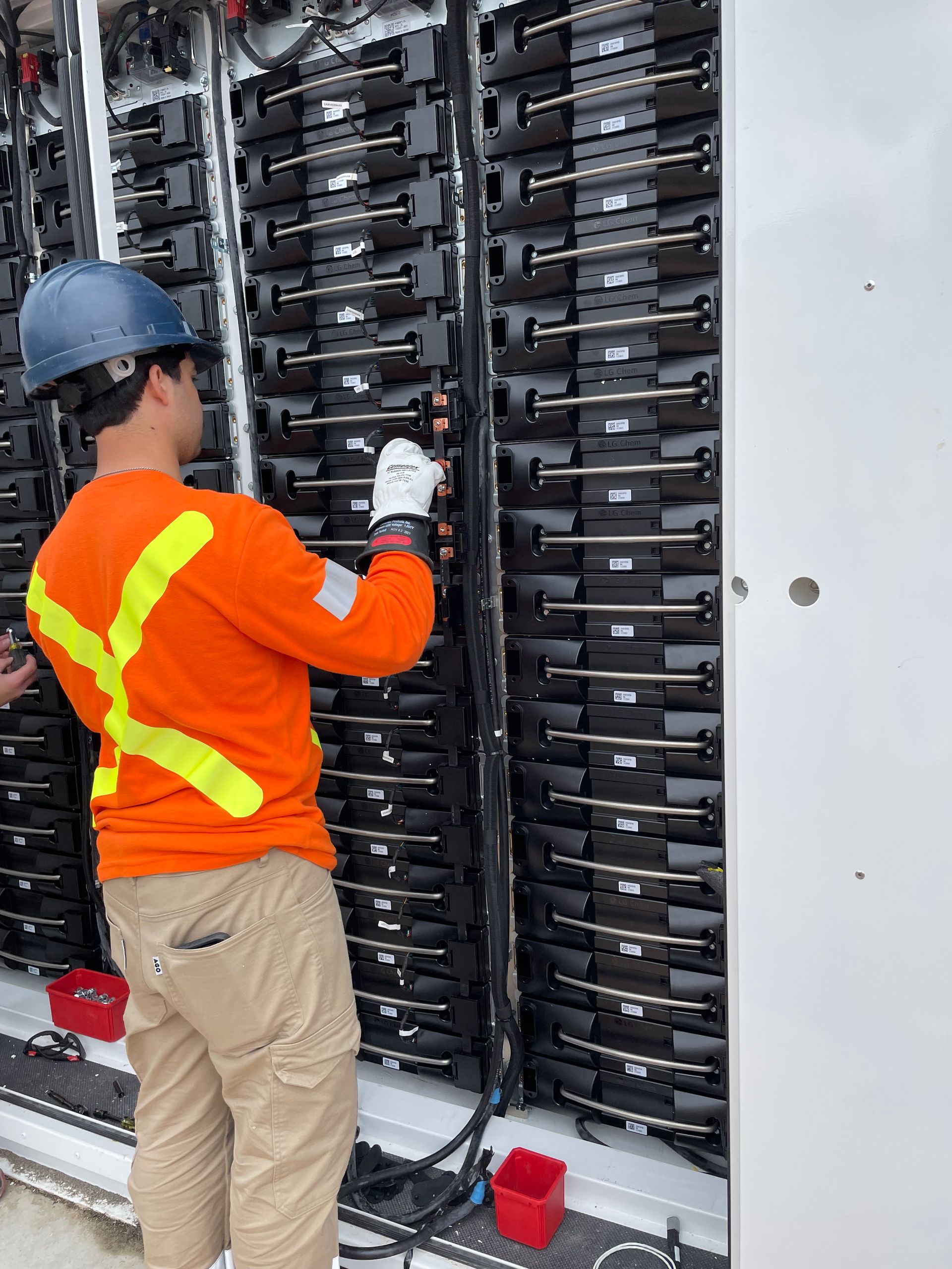 A man wearing a hard hat and an orange shirt is working on a server.