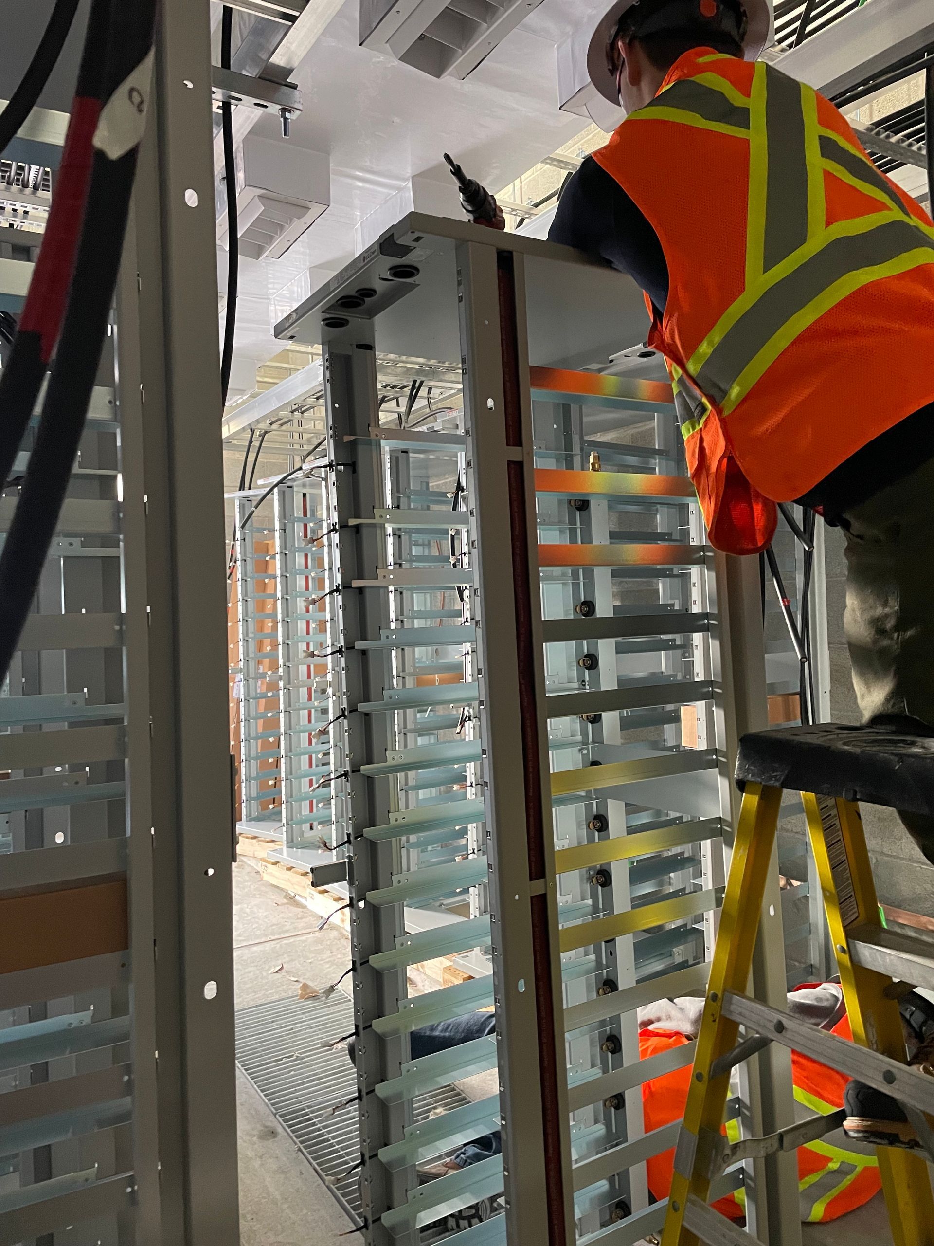 A man in an orange vest is standing on a ladder working on a machine.