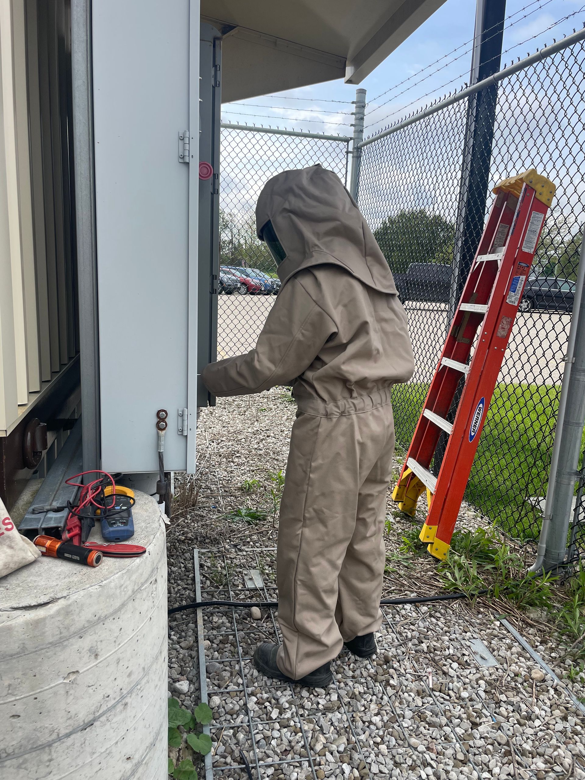 A man in a bee suit is working on a door next to a ladder.