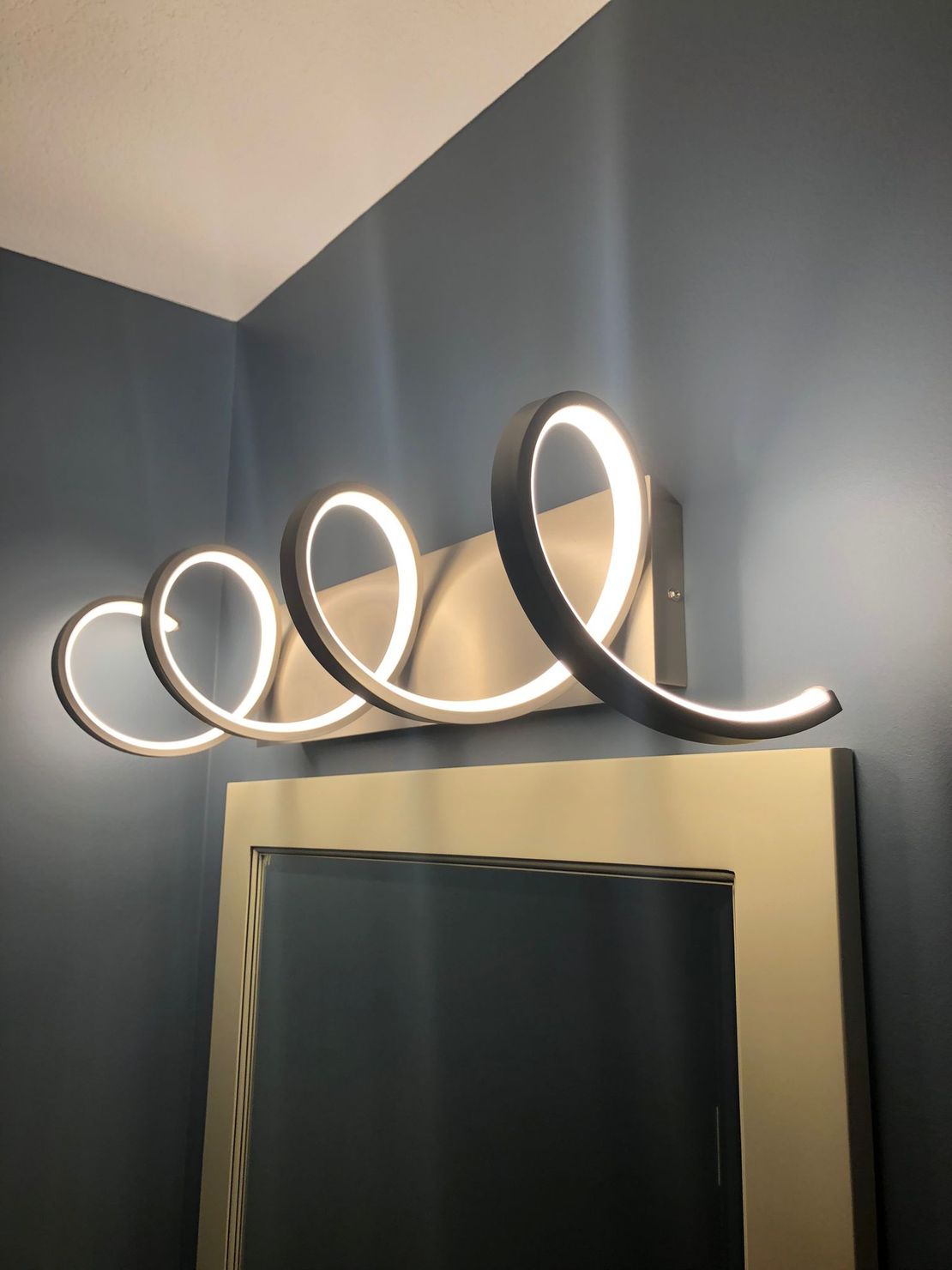 A bathroom vanity light with a spiral design is hanging above a mirror.