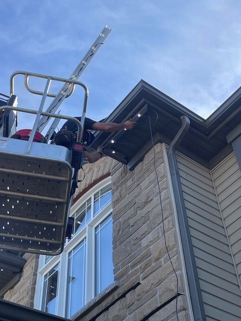 Person on a lift installing lights on a house's roofline.
