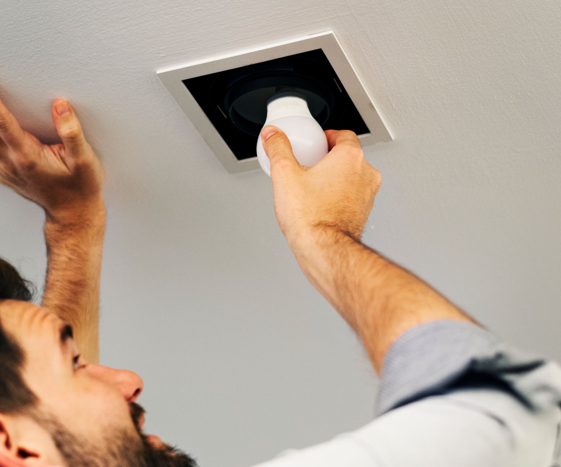 A man is installing a light bulb in the ceiling